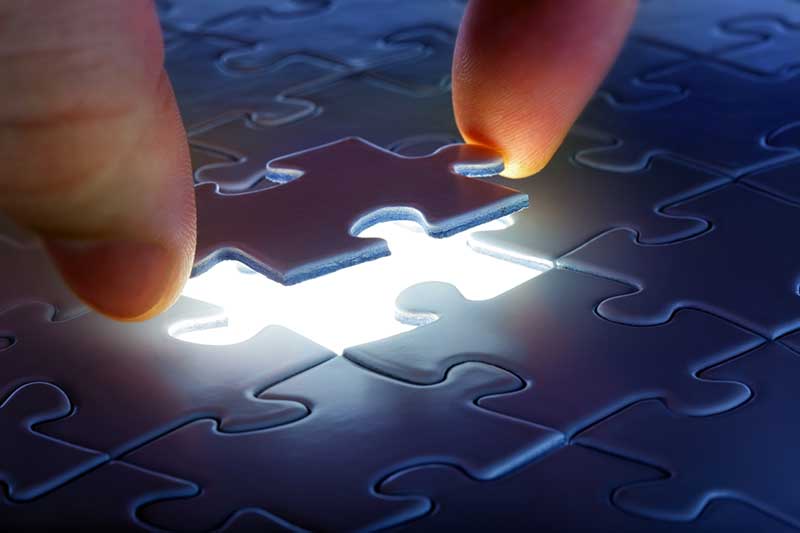 A white man's hand putting the last puzzle piece into a glowing puzzle.
